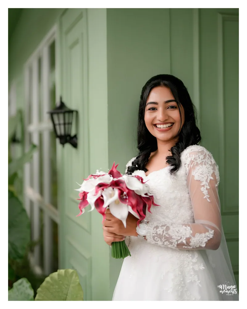 A bride smiling with her bouquet outside a pale green building