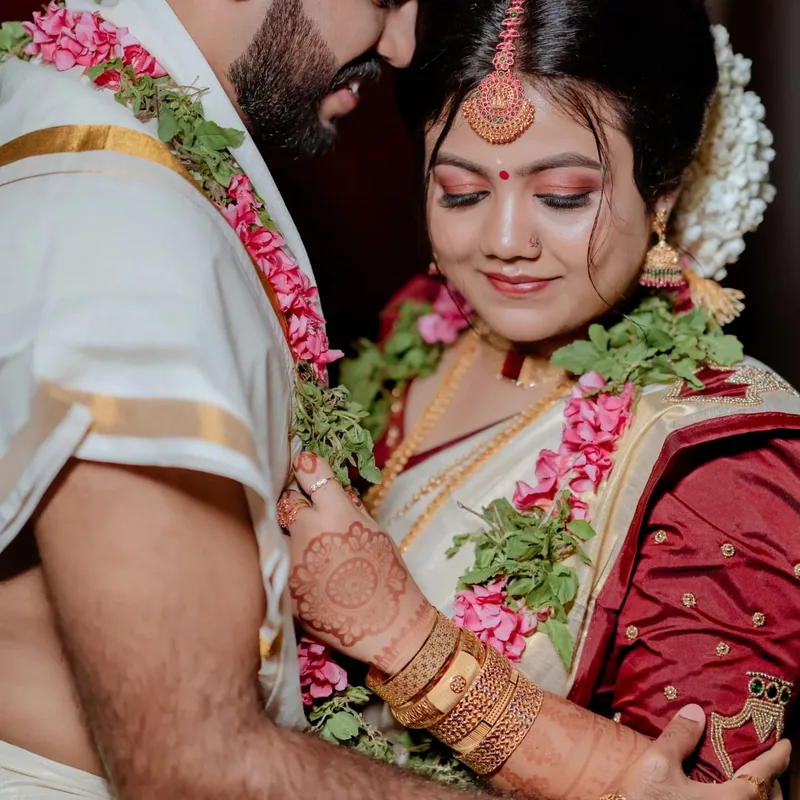 A wedding couple leaning together, wearing colourful flower garlands