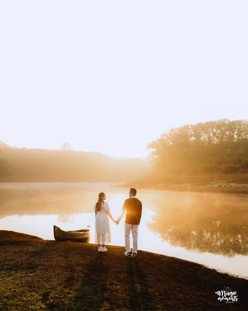 A couple holding hands beside a river in golden light