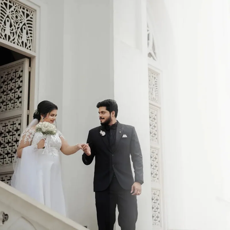 A groom kissing a bride’s hand beside a white building